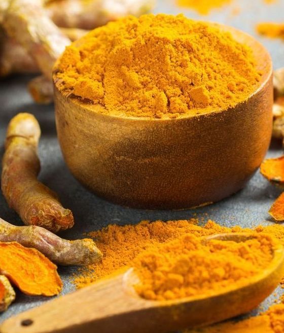Turmeric powder in a wooden scoop with turmeric roots on a dark surface
