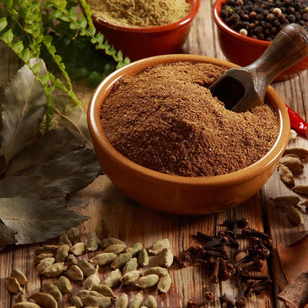 Wooden bowl of ground spice with spices around on a wooden surface