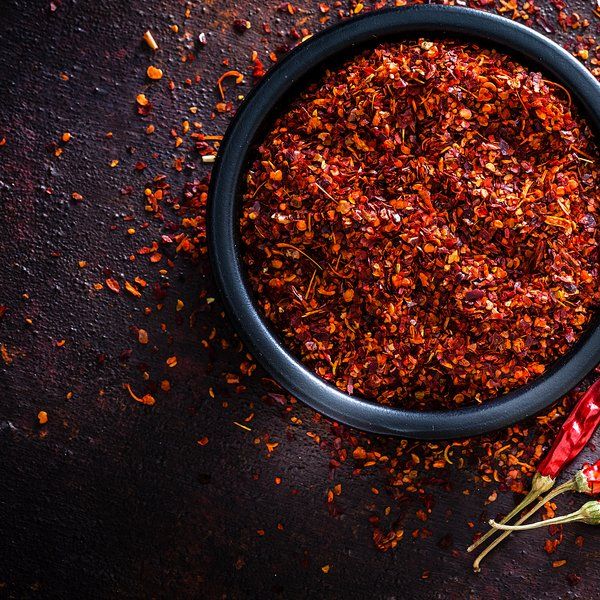 Black bowl filled with red chili flakes on a dark surface