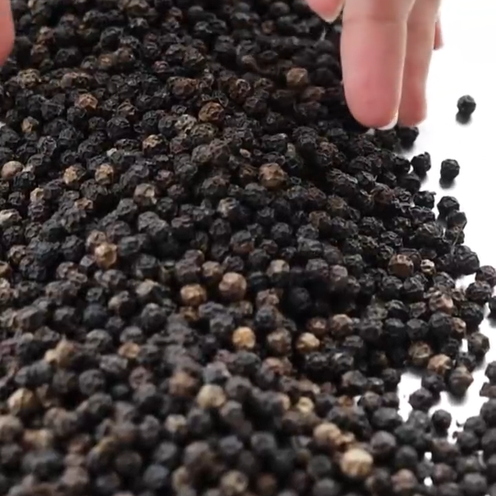 Hand reaching into a pile of black peppercorns